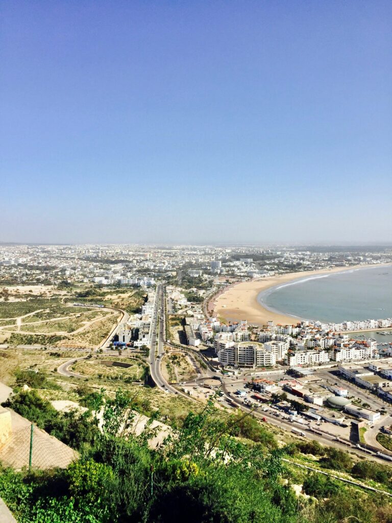 A stunning aerial view of an urban city with a sweeping coastline and busy roads, captured under a clear blue sky.