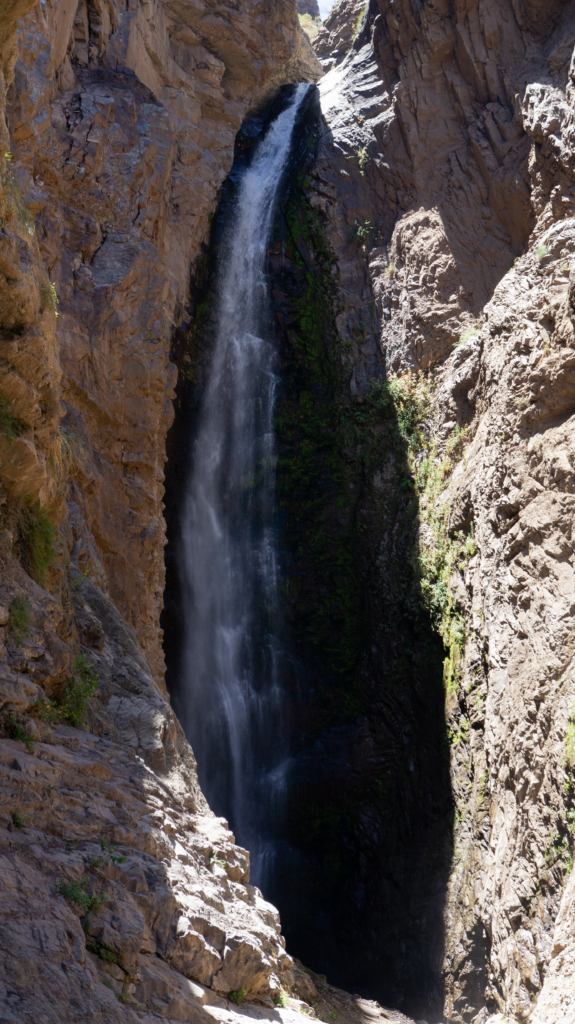 Vertical shot of a stunning waterfall flowing through rugged cliffs in bright sunlight.