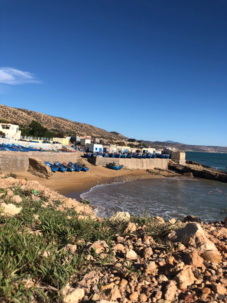 Charming coastal village with boats and rocky beach under clear skies in Tamri, Morocco.
