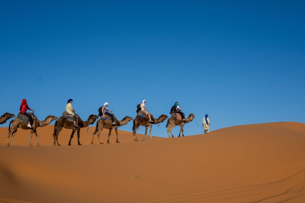 A group of people riding camels through the picturesque desert dunes under a clear blue sky.