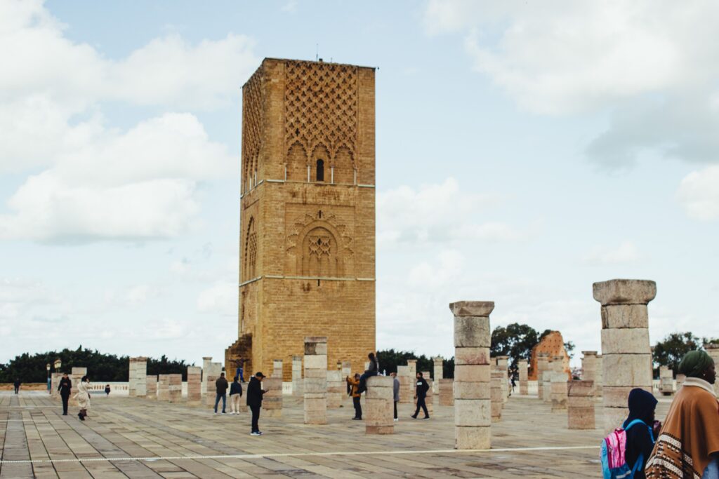 Visitors exploring the historical Hassan Tower in Rabat, Morocco, under a partly cloudy sky.