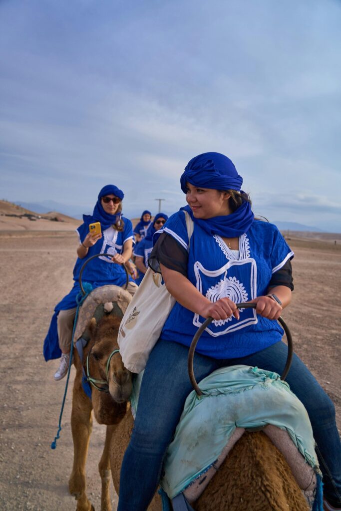 Group enjoying a camel ride in the Moroccan desert, wearing traditional attire.