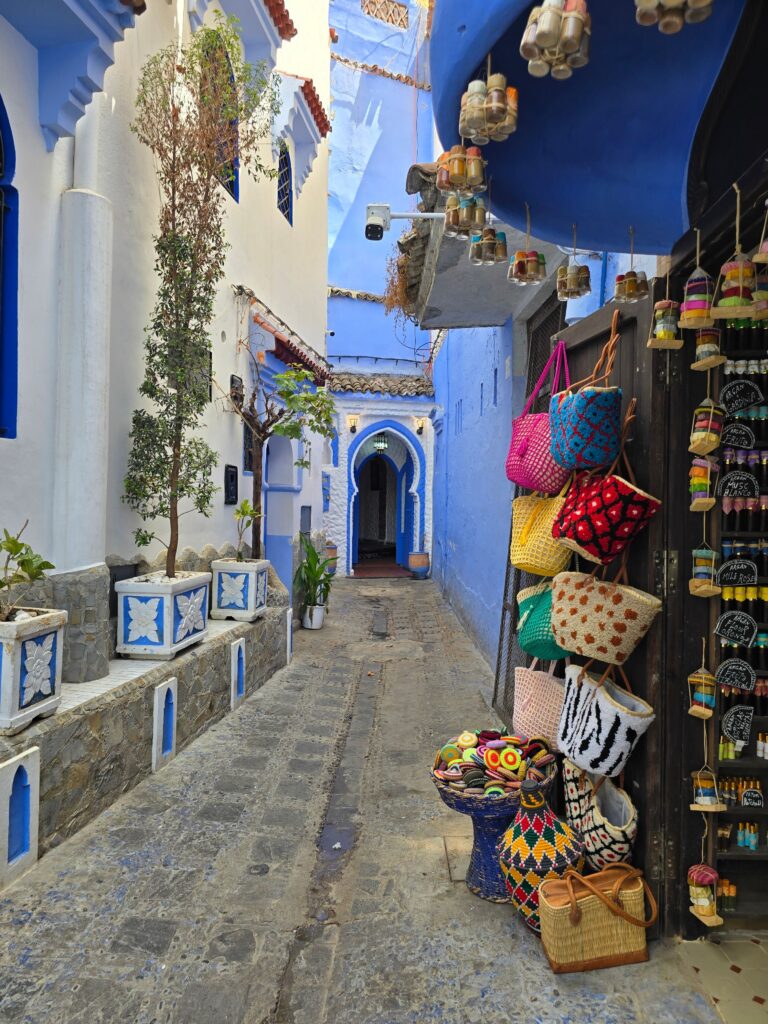 Vibrant display of woven bags in a blue alley in Chefchaouen, famed for its blue-painted buildings.