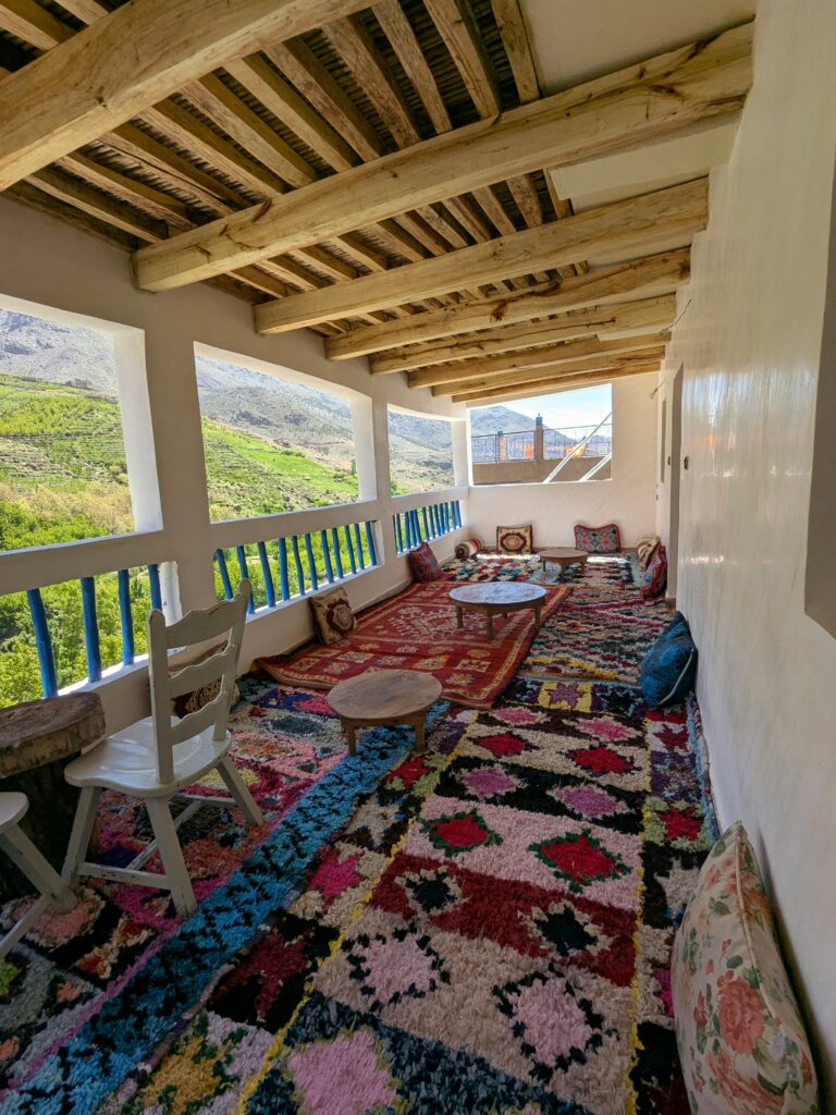 A colorful Moroccan terrace in Tachdirt, showcasing traditional rugs and mountain views.